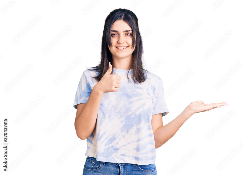 Young beautiful girl wearing casual t shirt showing palm hand and doing ok gesture with thumbs up, smiling happy and cheerful Young beautiful girl wearing casual t shirt showing palm hand and doing ok gesture with thumbs up, smiling happy and cheerful