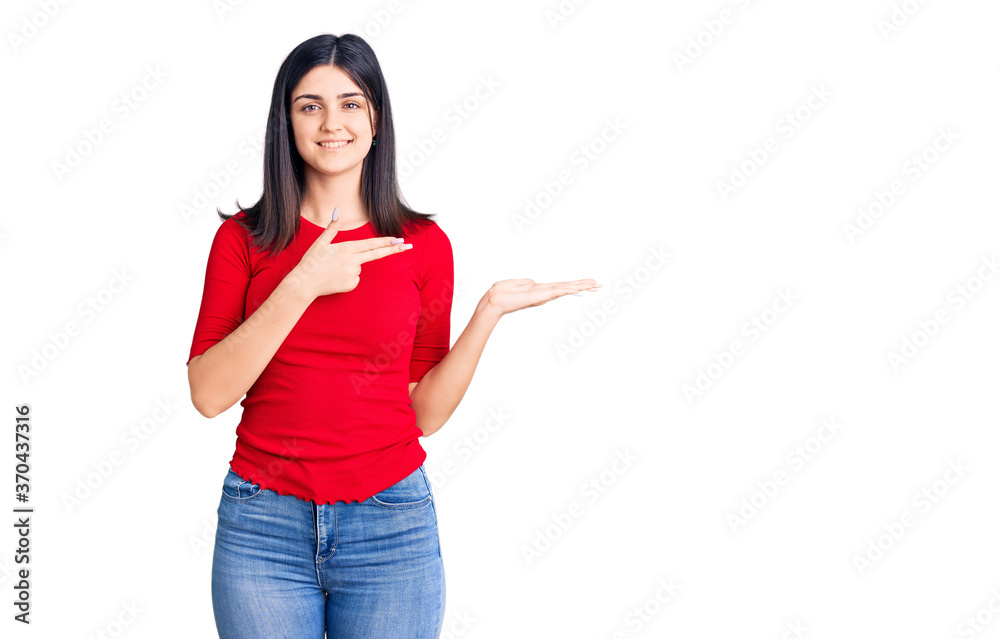 Young beautiful girl wearing casual t shirt amazed and smiling to the camera while presenting with hand and pointing with finger. Young beautiful girl wearing casual t shirt amazed and smiling to the camera while presenting with hand and pointing with finger.