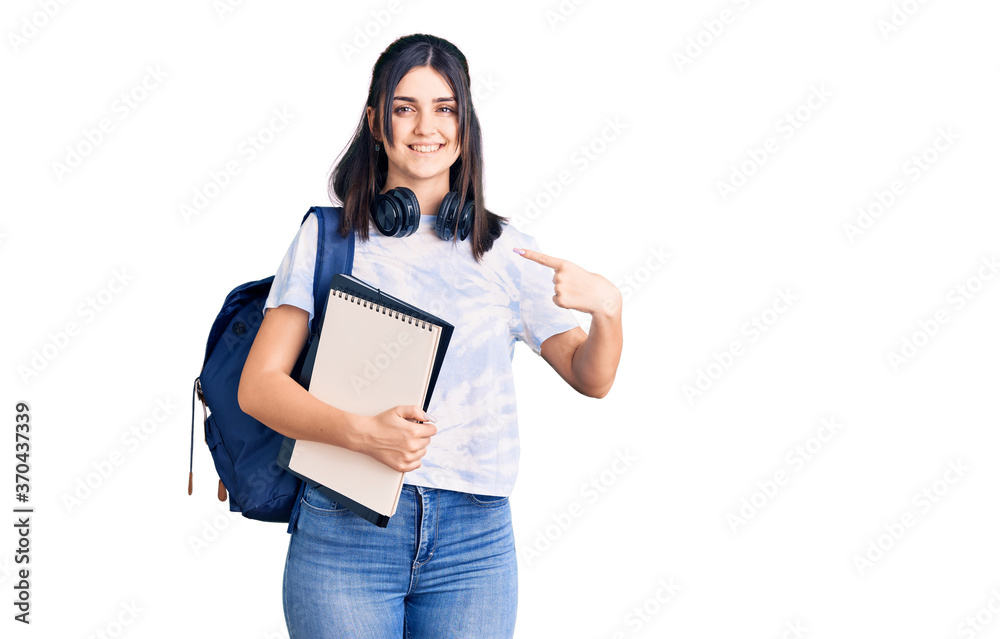 Young beautiful girl wearing student backpack holding notebook pointing finger to one self smiling happy and proud