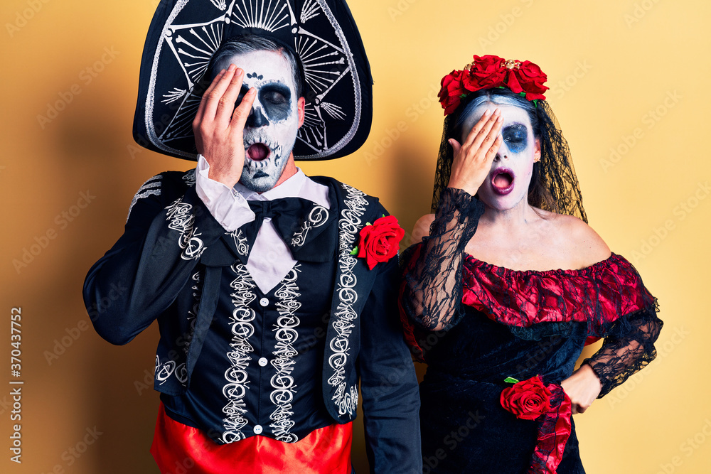 Young couple wearing mexican day of the dead costume over yellow yawning tired covering half face, eye and mouth with hand. face hurts in pain.