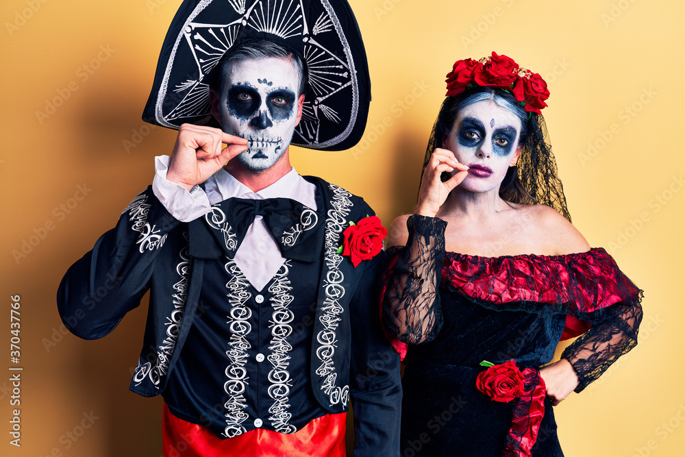 Obraz premium Young couple wearing mexican day of the dead costume over yellow mouth and lips shut as zip with fingers. secret and silent, taboo talking