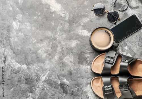 Cup of coffee with shoes, mobile phone and sunglasses on grey background