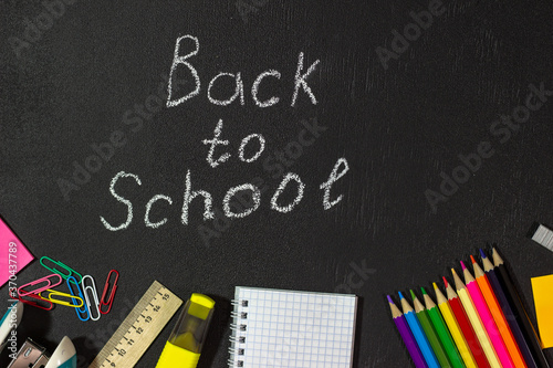 Back to school. Written in white chalk on a chalk board. Black background, sharp black texture.