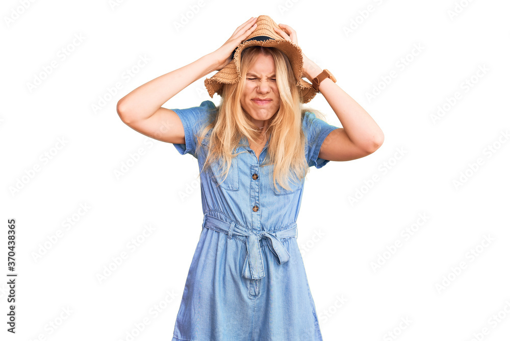 Young beautiful blonde woman wearing summer hat and dress suffering from headache desperate and stressed because pain and migraine. hands on head. Young beautiful blonde woman wearing summer hat and dress suffering from headache desperate and stressed because pain and migraine. hands on head.