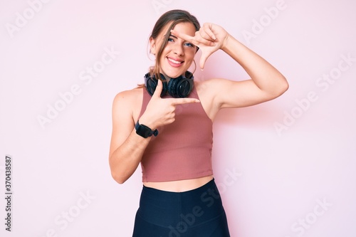 Beautiful young caucasian woman wearing gym clothes and using headphones smiling making frame with hands and fingers with happy face. creativity and photography concept.