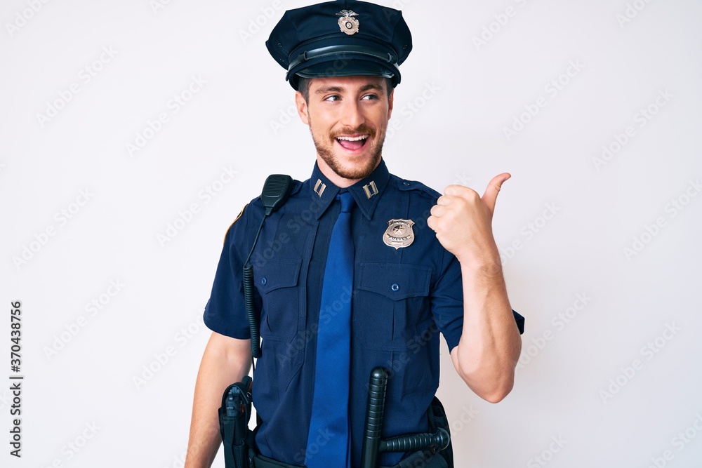 Young caucasian man wearing police uniform smiling with happy face looking and pointing to the side with thumb up. Young caucasian man wearing police uniform smiling with happy face looking and pointing to the side with thumb up.