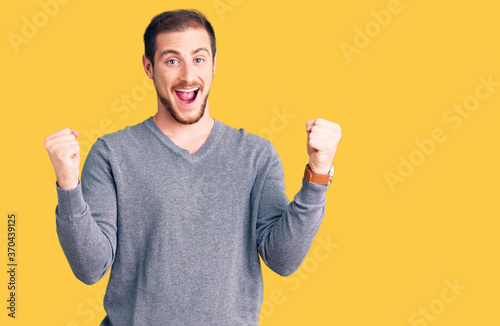 Young handsome caucasian man wearing casual winter sweater screaming proud, celebrating victory and success very excited with raised arms