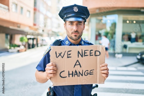 Young handsome hispanic policeman wearing police uniform with serious expression holding we need a change banner at town street © Krakenimages.com