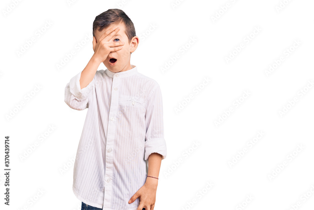 Cute blond kid wearing elegant shirt peeking in shock covering face and eyes with hand, looking through fingers with embarrassed expression. Cute blond kid wearing elegant shirt peeking in shock covering face and eyes with hand, looking through fingers with embarrassed expression.