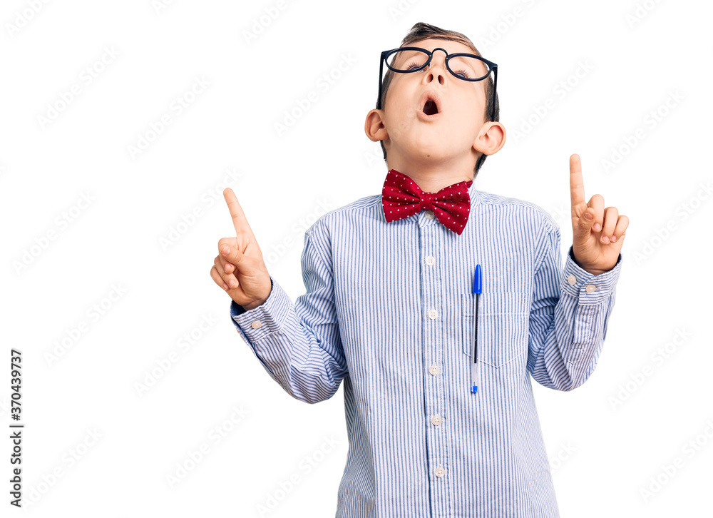 Cute blond kid wearing nerd bow tie and glasses amazed and surprised looking up and pointing with fingers and raised arms. Cute blond kid wearing nerd bow tie and glasses amazed and surprised looking up and pointing with fingers and raised arms.