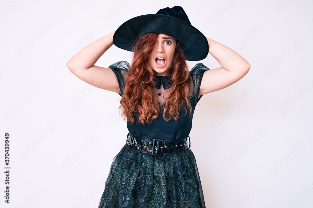 Young beautiful woman wearing witch halloween costume crazy and scared with hands on head, afraid and surprised of shock with open mouth Young beautiful woman wearing witch halloween costume crazy and scared with hands on head, afraid and surprised of shock with open mouth
