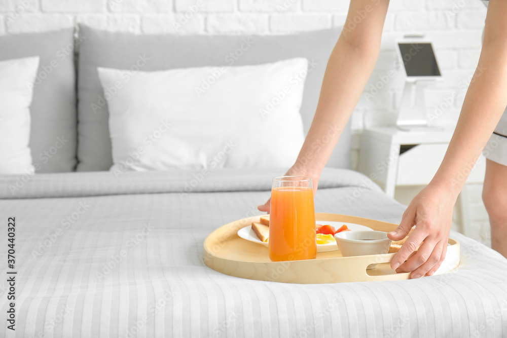 Chambermaid putting tasty breakfast on bed in hotel room Chambermaid putting tasty breakfast on bed in hotel room