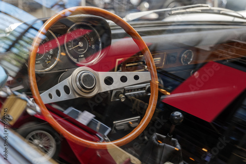 Selected focus at unique decorated shiny and wooden steering wheel and blur dashboard through car's window with reflection inside vintage classic old car. 