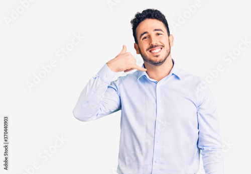 Young hispanic man wearing business clothes smiling doing phone gesture with hand and fingers like talking on the telephone. communicating concepts. © Krakenimages.com