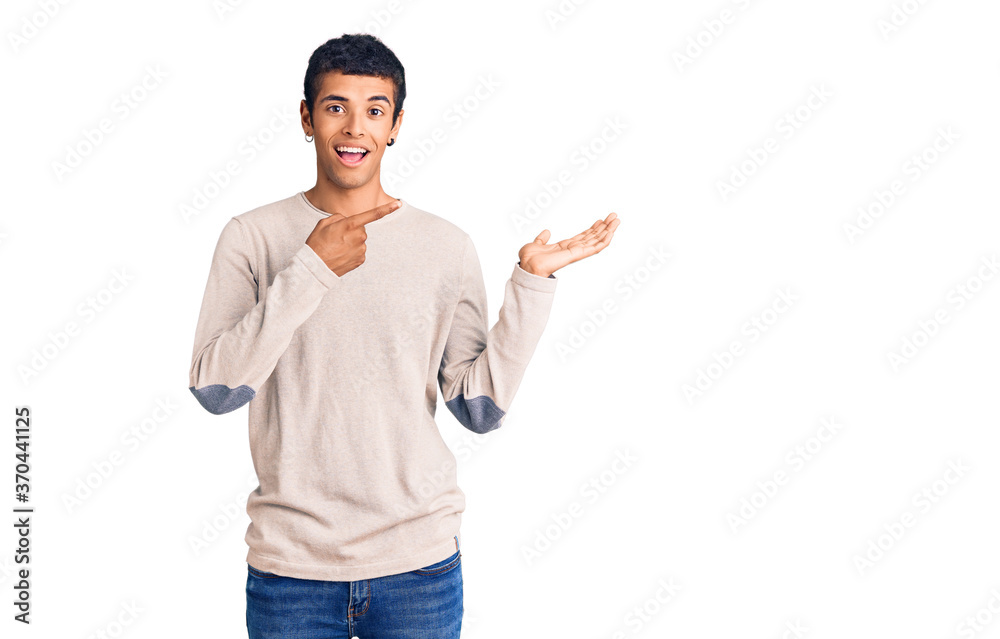 Young african amercian man wearing casual clothes amazed and smiling to the camera while presenting with hand and pointing with finger. Young african amercian man wearing casual clothes amazed and smiling to the camera while presenting with hand and pointing with finger.