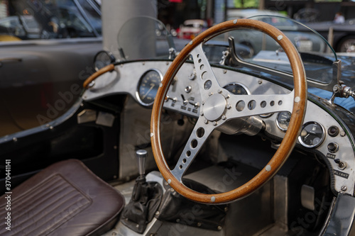 Selected focus at unique decorated shiny and wooden steering wheel and metallic dashboard inside vintage classic old sport car. 