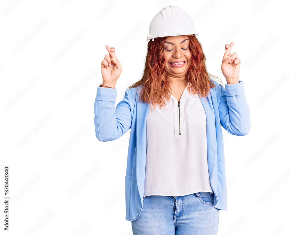 Young latin woman wearing architect hardhat gesturing finger crossed smiling with hope and eyes closed. luck and superstitious concept. Young latin woman wearing architect hardhat gesturing finger crossed smiling with hope and eyes closed. luck and superstitious concept.