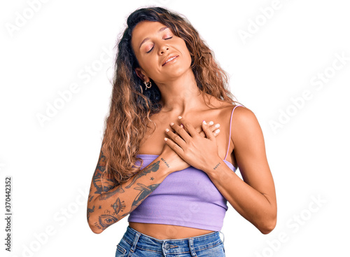 Young hispanic woman with tattoo wearing casual clothes smiling with hands on chest with closed eyes and grateful gesture on face. health concept. © Krakenimages.com