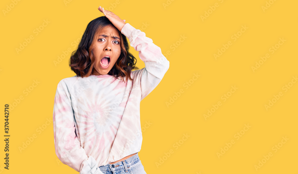 Young beautiful mixed race woman wearing casual tie dye sweatshirt surprised with hand on head for mistake, remember error. forgot, bad memory concept. Young beautiful mixed race woman wearing casual tie dye sweatshirt surprised with hand on head for mistake, remember error. forgot, bad memory concept.