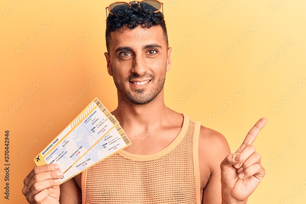 Young hispanic man holding boarding pass smiling happy pointing with hand and finger to the side Young hispanic man holding boarding pass smiling happy pointing with hand and finger to the side