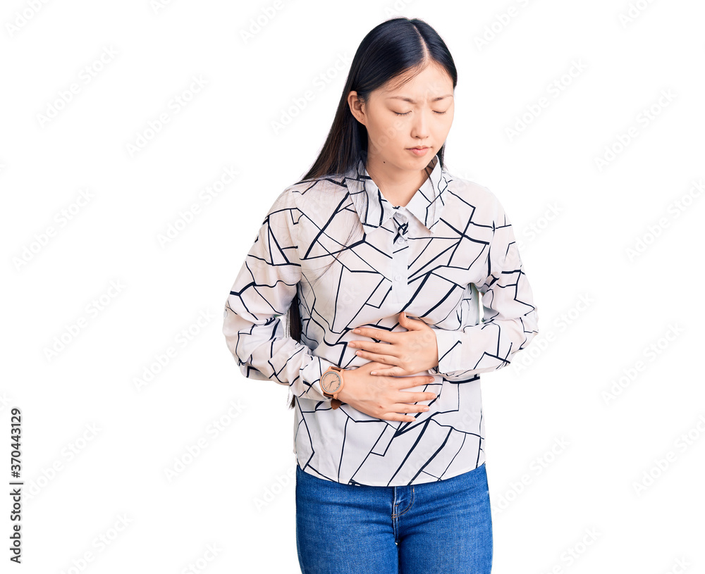 Young beautiful chinese woman wearing casual shirt with hand on stomach because indigestion, painful illness feeling unwell. ache concept. Young beautiful chinese woman wearing casual shirt with hand on stomach because indigestion, painful illness feeling unwell. ache concept.
