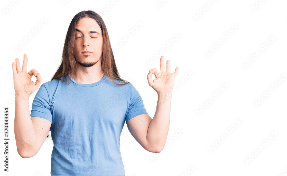 Young adult man with long hair wearing casual clothes relax and smiling with eyes closed doing meditation gesture with fingers. yoga concept. Young adult man with long hair wearing casual clothes relax and smiling with eyes closed doing meditation gesture with fingers. yoga concept.