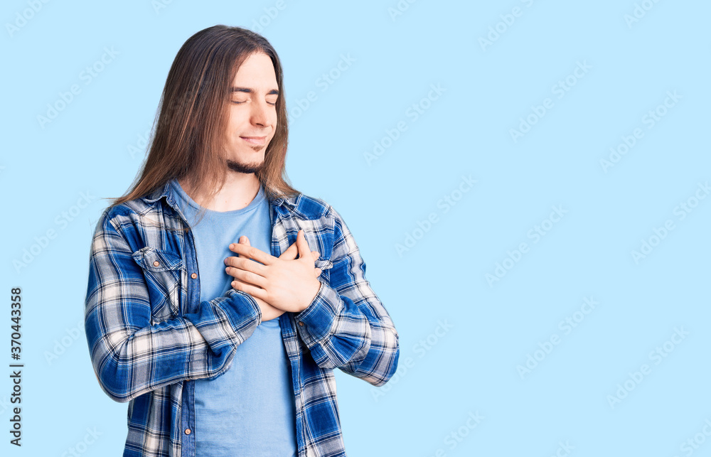 Young adult man with long hair wearing casual shirt smiling with hands on chest with closed eyes and grateful gesture on face. health concept.