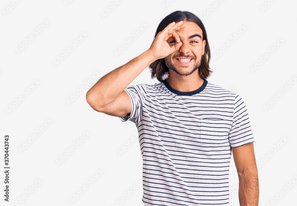 Young handsome man wearing casual clothes doing ok gesture with hand smiling, eye looking through fingers with happy face. Young handsome man wearing casual clothes doing ok gesture with hand smiling, eye looking through fingers with happy face.