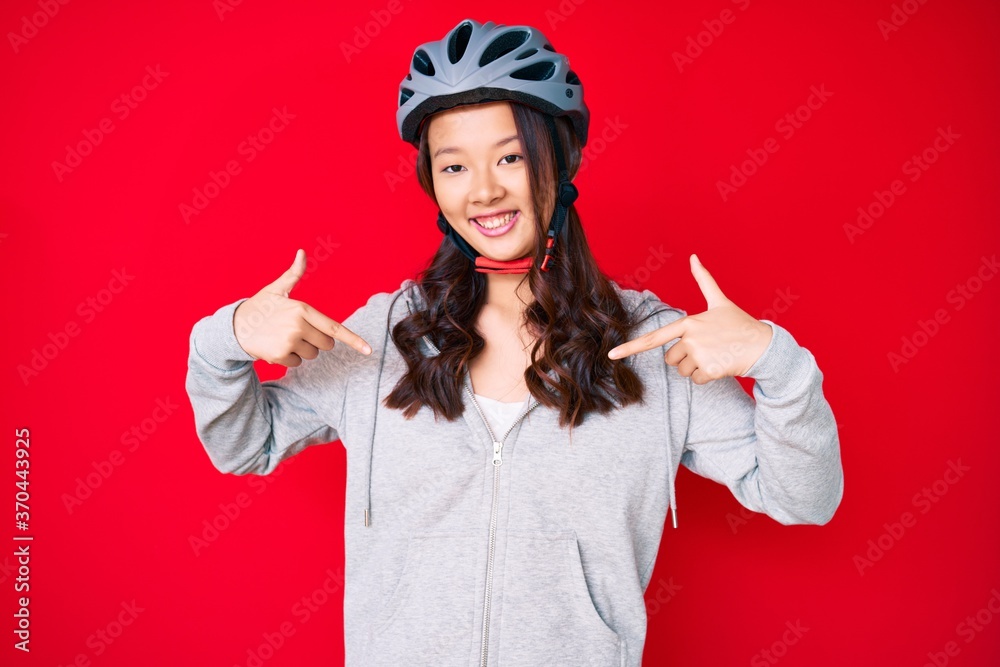 Young beautiful chinese girl wearing bike helmet looking confident with smile on face, pointing oneself with fingers proud and happy. Young beautiful chinese girl wearing bike helmet looking confident with smile on face, pointing oneself with fingers proud and happy.