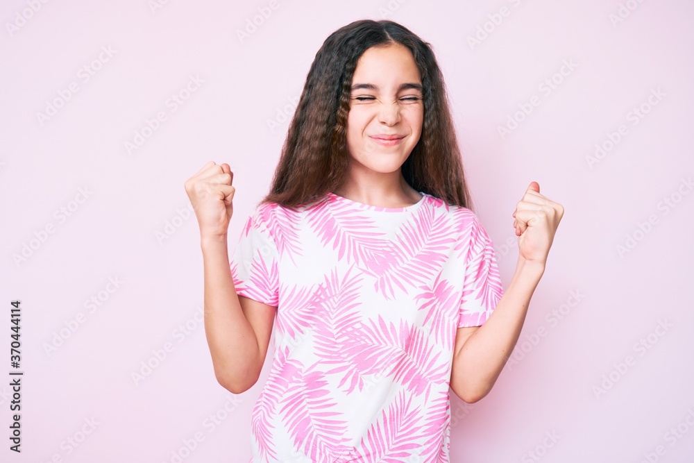 Cute hispanic child girl wearing casual clothes very happy and excited doing winner gesture with arms raised, smiling and screaming for success. celebration concept.