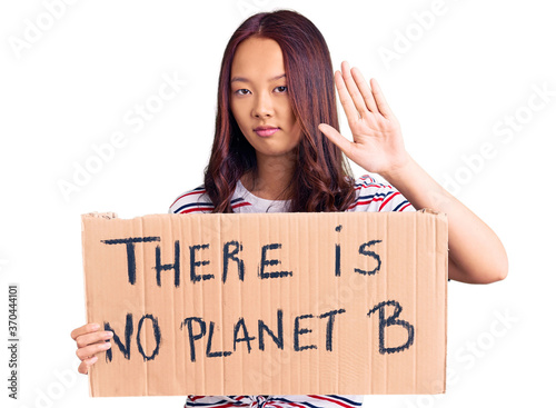 Young beautiful chinese girl holding there is no planet b banner with open hand doing stop sign with serious and confident expression, defense gesture © Krakenimages.com