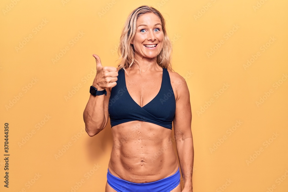 Middle age caucasian blonde woman wearing bikini smiling happy and positive, thumb up doing excellent and approval sign Middle age caucasian blonde woman wearing bikini smiling happy and positive, thumb up doing excellent and approval sign