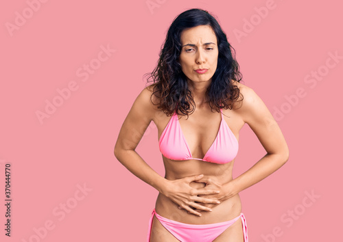 Young beautiful hispanic woman wearing bikini with hand on stomach because indigestion  painful illness feeling unwell. ache concept.