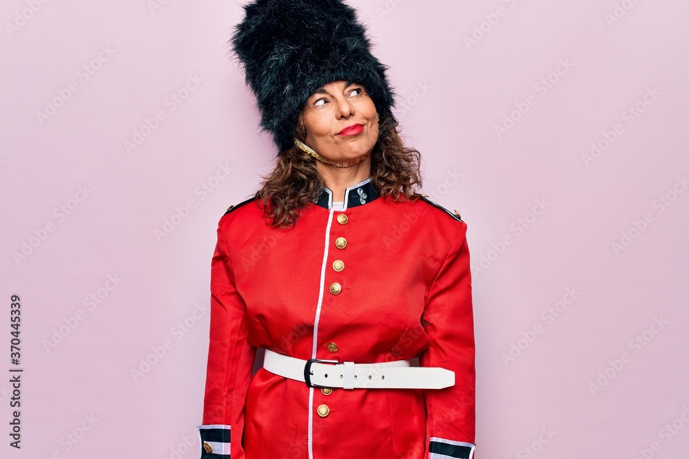 Middle age beautiful wales guard woman wearing traditional uniform over pink background smiling looking to the side and staring away thinking.