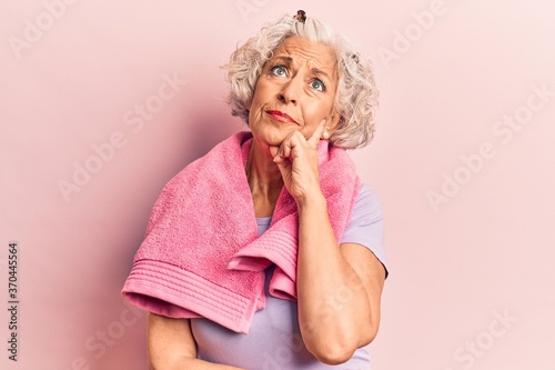 Senior grey-haired woman wearing sportswear and towel thinking concentrated about doubt with finger on chin and looking up wondering