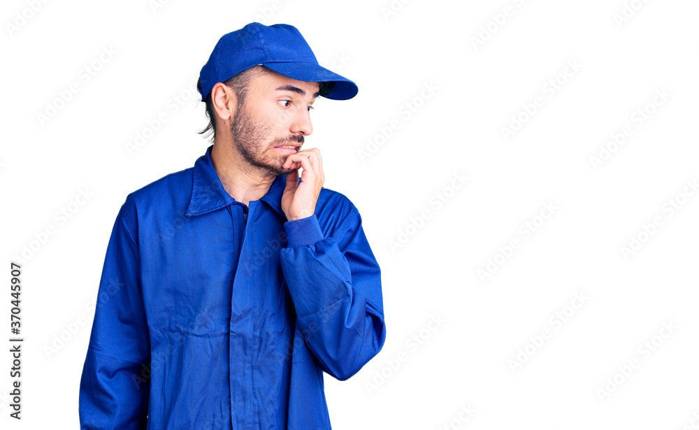 Young hispanic man wearing painter uniform looking stressed and nervous with hands on mouth biting nails. anxiety problem. Young hispanic man wearing painter uniform looking stressed and nervous with hands on mouth biting nails. anxiety problem.