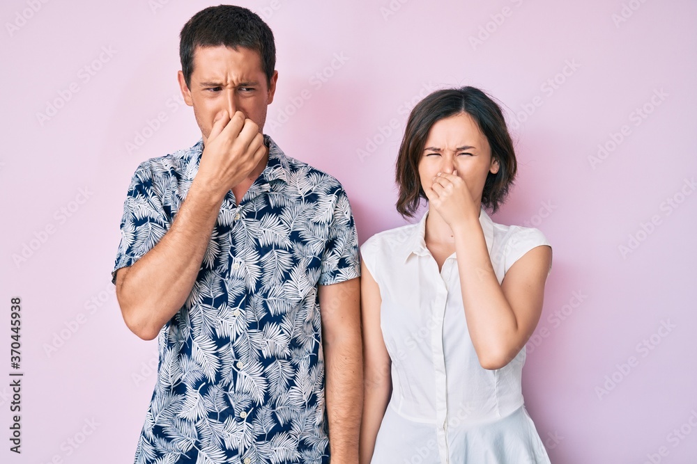 Beautiful couple wearing casual clothes smelling something stinky and disgusting, intolerable smell, holding breath with fingers on nose. bad smell Beautiful couple wearing casual clothes smelling something stinky and disgusting, intolerable smell, holding breath with fingers on nose. bad smell