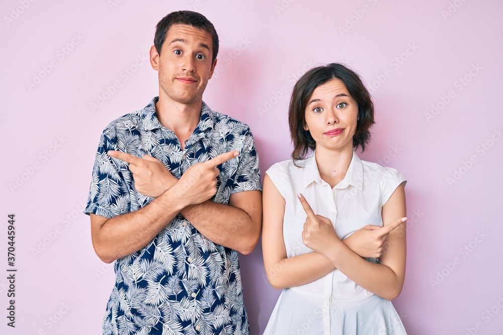Beautiful couple wearing casual clothes pointing to both sides with fingers, different direction disagree Beautiful couple wearing casual clothes pointing to both sides with fingers, different direction disagree