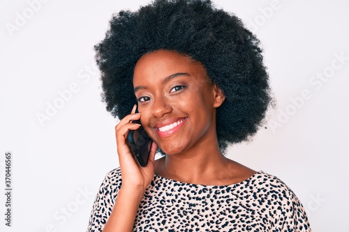 Young african american woman having conversation talking on the smartphone looking positive and happy standing and smiling with a confident smile showing teeth