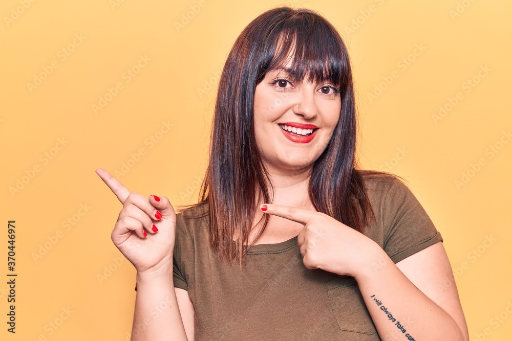 Young plus size woman wearing casual clothes smiling and looking at the camera pointing with two hands and fingers to the side.