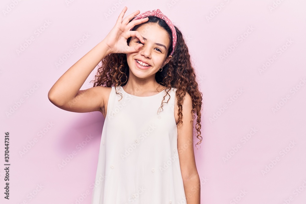 Beautiful kid girl with curly hair wearing casual clothes smiling happy doing ok sign with hand on eye looking through fingers Beautiful kid girl with curly hair wearing casual clothes smiling happy doing ok sign with hand on eye looking through fingers