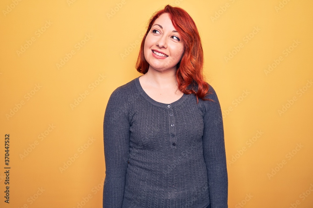 Obraz premium Young beautiful redhead woman wearing casual sweater standing over yellow background looking to side, relax profile pose with natural face and confident smile.
