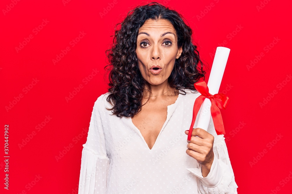 Middle age beautiful woman holding graduate degree diploma scared and amazed with open mouth for surprise, disbelief face Middle age beautiful woman holding graduate degree diploma scared and amazed with open mouth for surprise, disbelief face