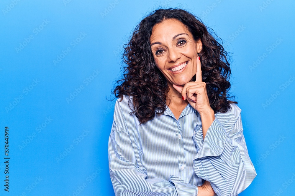 Middle age beautiful woman wearing casual shirt smiling looking confident at the camera with crossed arms and hand on chin. thinking positive.