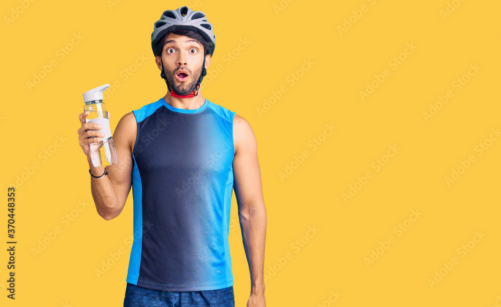 Handsome hispanic man wearing bike helmet and holding water bottle scared and amazed with open mouth for surprise, disbelief face Handsome hispanic man wearing bike helmet and holding water bottle scared and amazed with open mouth for surprise, disbelief face