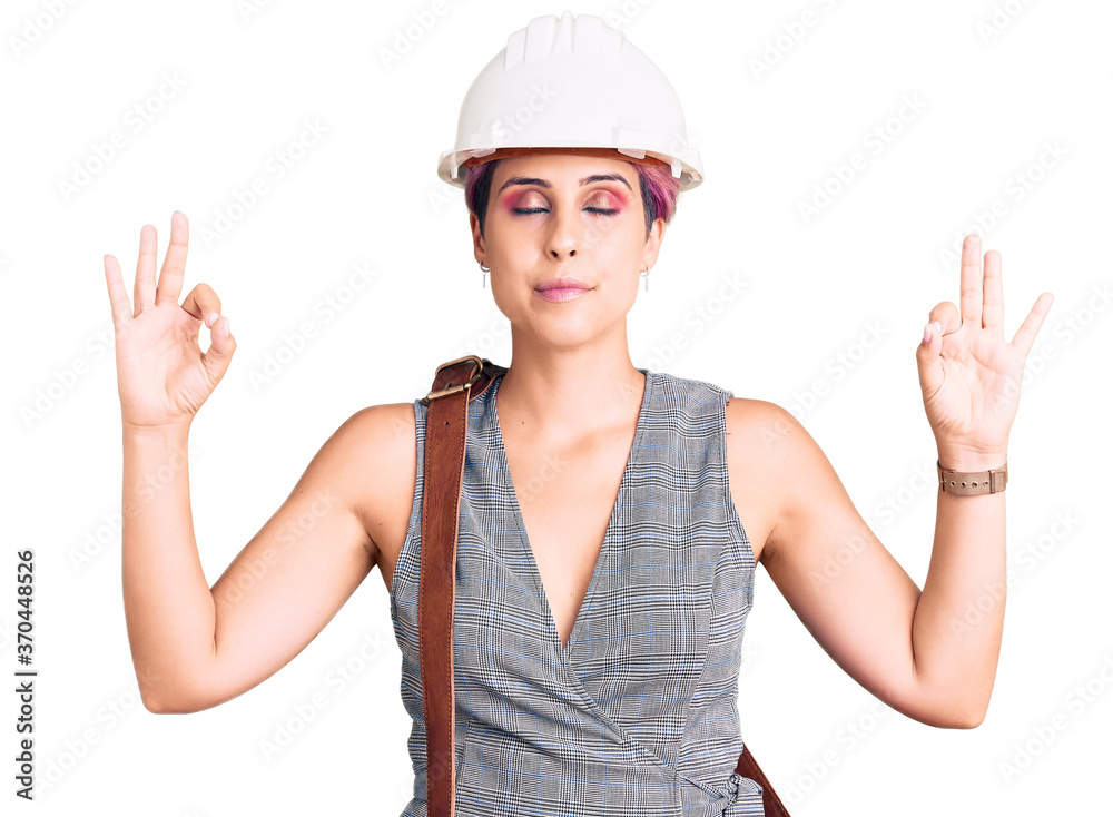 Young beautiful woman wearing architect hardhat and leather bag relax and smiling with eyes closed doing meditation gesture with fingers. yoga concept. Young beautiful woman wearing architect hardhat and leather bag relax and smiling with eyes closed doing meditation gesture with fingers. yoga concept.