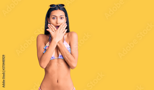 Young beautiful latin girl wearing bikini and sunglasses shocked covering mouth with hands for mistake. secret concept.