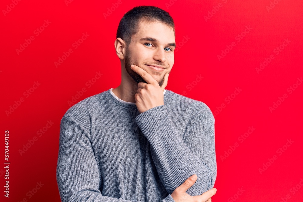 Young handsome man wearing casual sweater smiling looking confident at the camera with crossed arms and hand on chin. thinking positive. Young handsome man wearing casual sweater smiling looking confident at the camera with crossed arms and hand on chin. thinking positive.