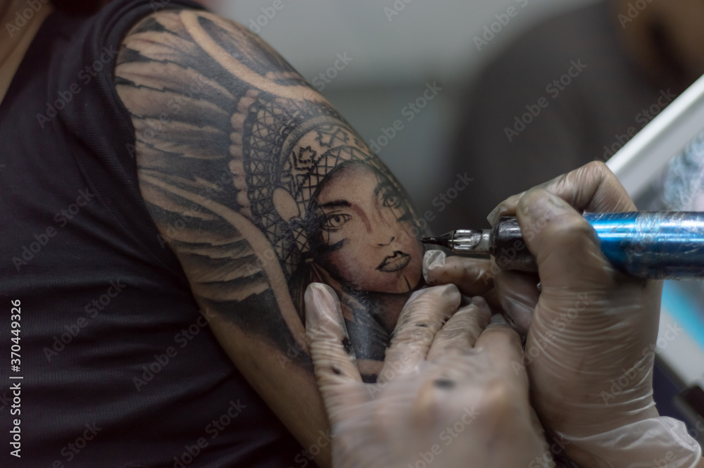 Closeup shot tattoo artist holding a tattoo machine tattooing a person