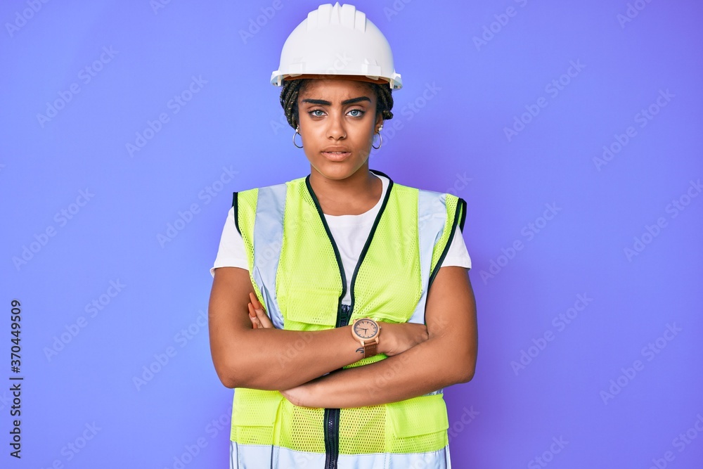 Young african american woman with braids wearing safety helmet and reflective jacket skeptic and nervous, disapproving expression on face with crossed arms. negative person. Young african american woman with braids wearing safety helmet and reflective jacket skeptic and nervous, disapproving expression on face with crossed arms. negative person.